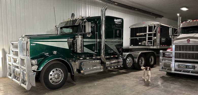 Lee-Lubbers-semi-dog-South-Dakota A brown and white dog in the shop with green semi trucks