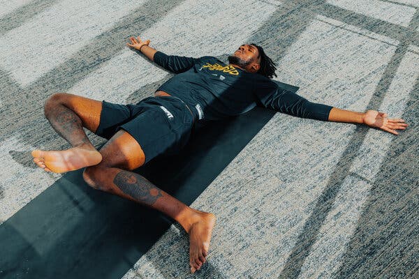 Looney lies on his yoga mat with his arms out and his knees bent and his right foot over his left knee.