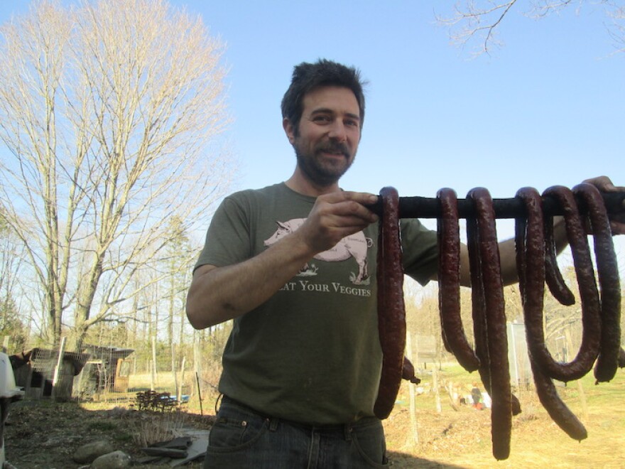  A man holding a stick with lots of sausages hanging from it.