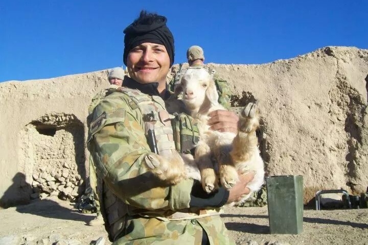 IMAGE of a man in the army holding a goat. 