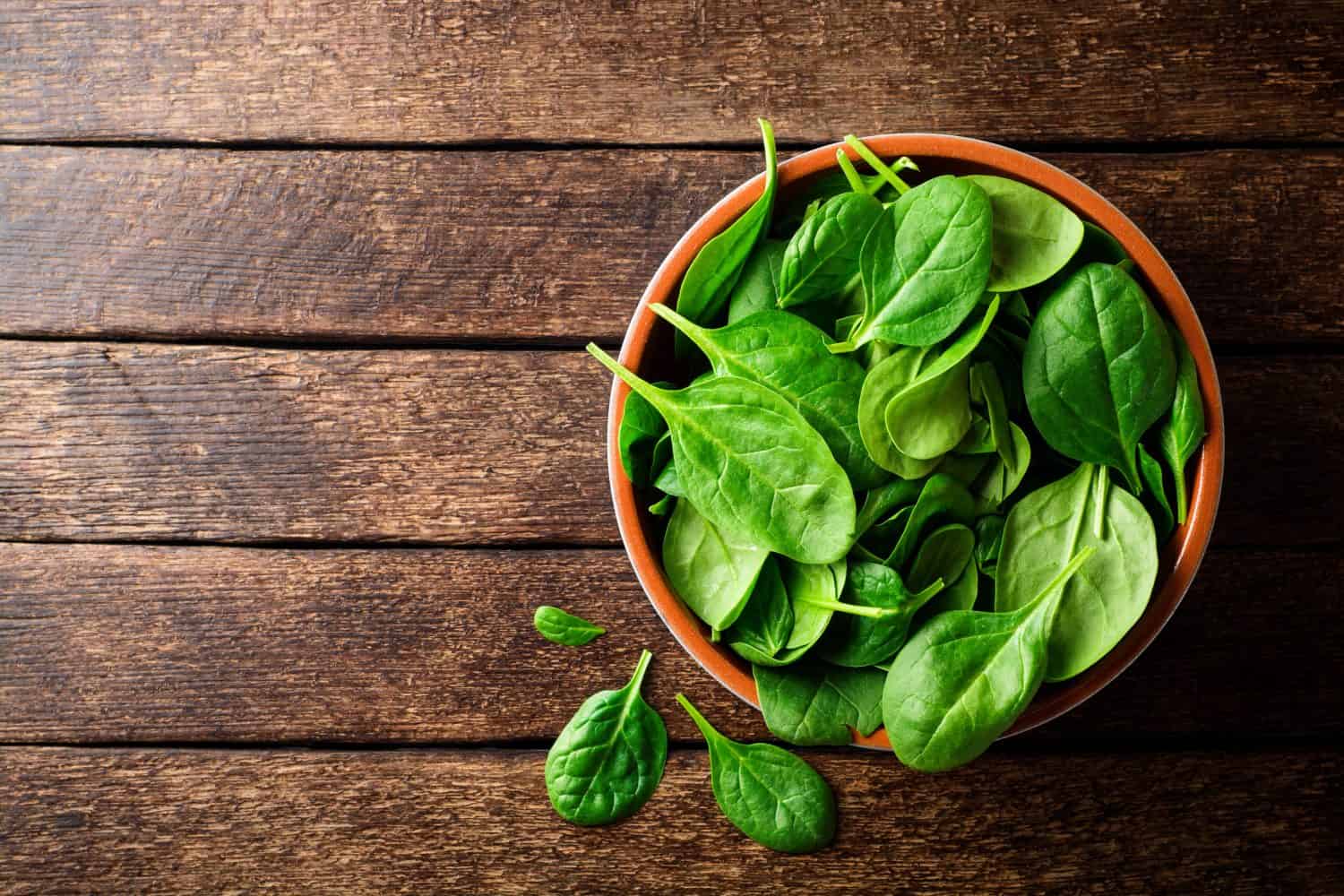 Fresh spinach leaves in bowl on rustic wooden table. Top view.