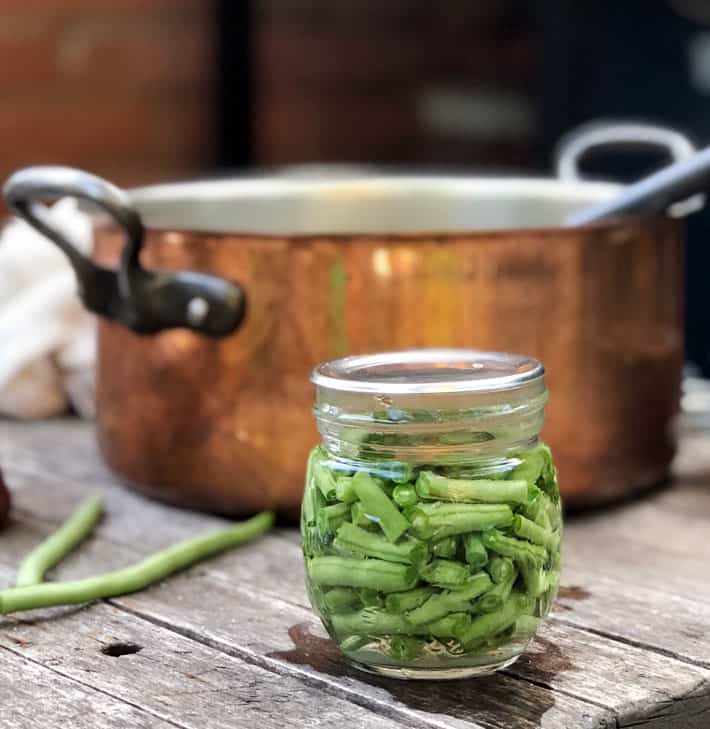 Home canned green beans in a mason jar with copper pot.
