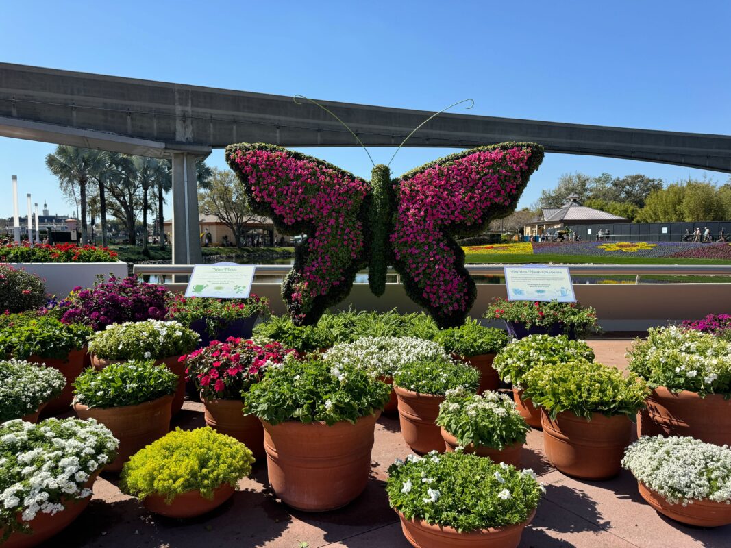 A pink butterfly topiary surrounded by potted plants.
